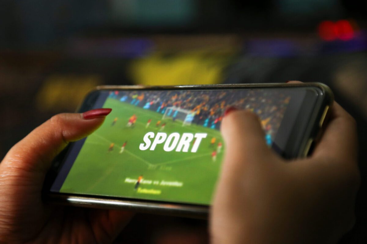 hands showing sport video on a smart phone | diario-economia.com Close-up of hands holding a smartphone showing a soccer game with the word SPORT on the screen