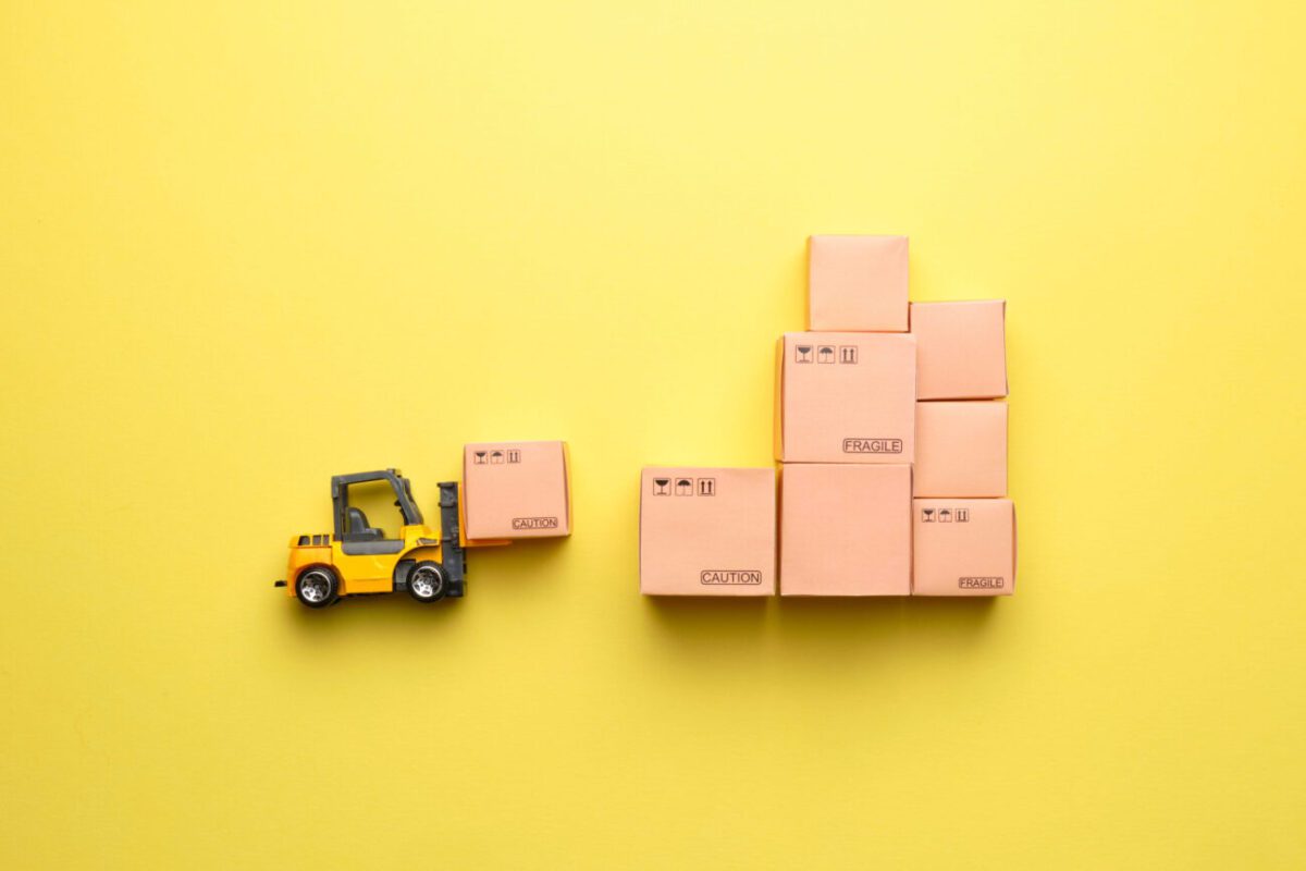 Toy yellow forklift moving a box toward a stack of fragile boxes on a yellow background.