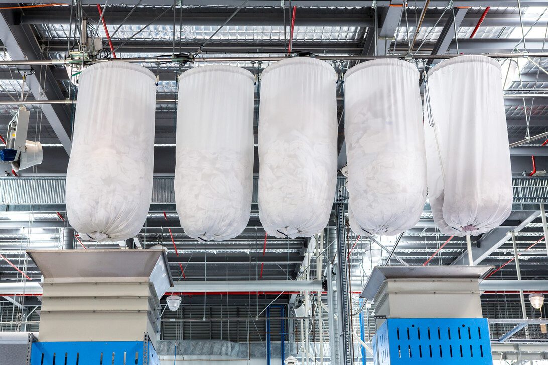 clothes in Cloth bag are being conveyed to washing machine | diario-economia.com Row of large white fabric filter bags hanging from a metal frame in a factory dust collection system.