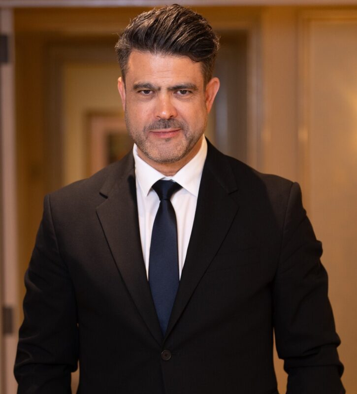 MH_PHOTOGRAPHY | diario-economia.com Man in a black suit with white shirt and navy tie stands in a hallway, looking at the camera with a slight smile.