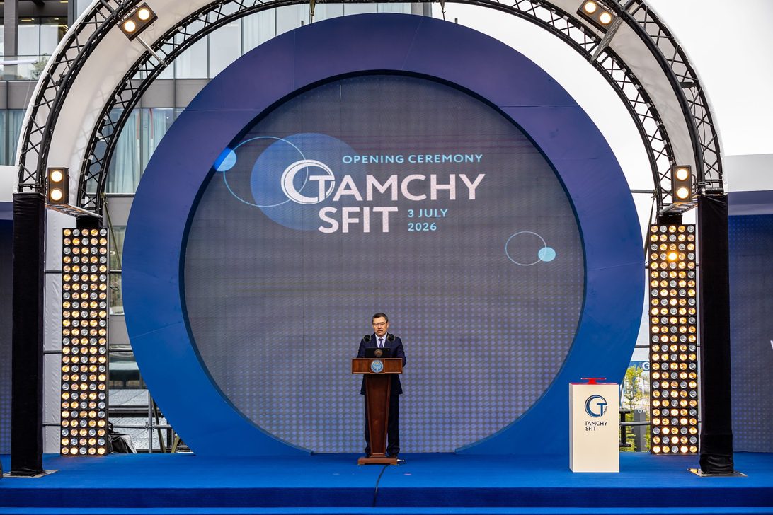 Tamchy - IP | diario-economia.com Speaker at a podium on a blue circular-stage backdrop for the Opening Ceremony (text on screen reads 'Opening Ceremony GAMCHY SFIT 3 July 2026')