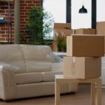 Living room with stacked cardboard boxes and a wrapped sofa, ready for moving.