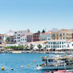 Harbor scene in a Mediterranean town with colorful buildings along the waterfront and boats anchored in calm blue water