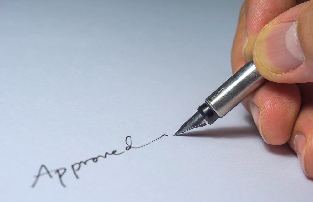 780577 - IRV Perito Calígrafo | diario-economia.com Close-up of a hand signing a document with a fountain pen, writing 'Approved'.