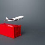 Toy airplane lifting off from a red shipping container on a gray background, illustrating air cargo.