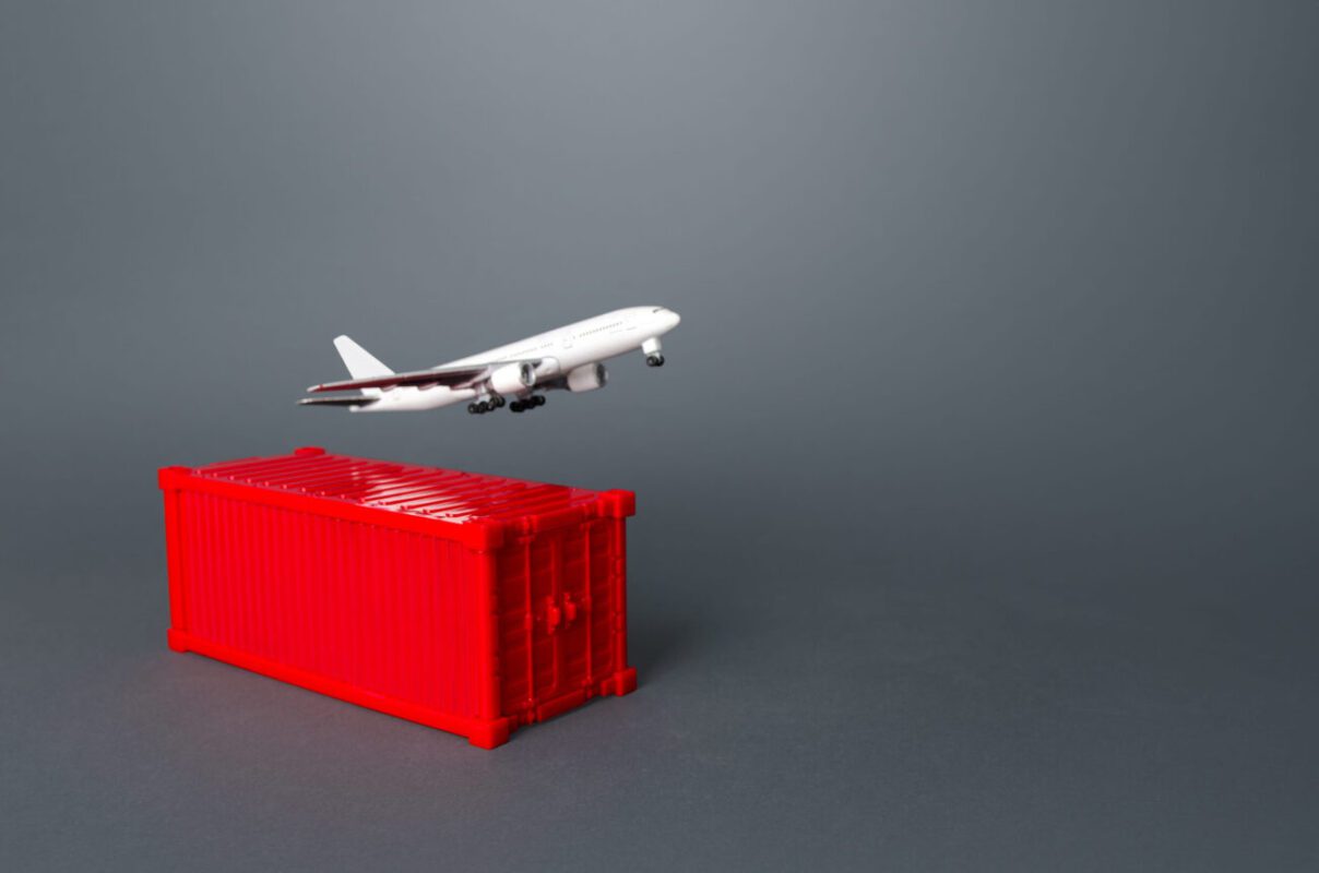 Toy airplane lifting off from a red shipping container on a gray background, illustrating air cargo.