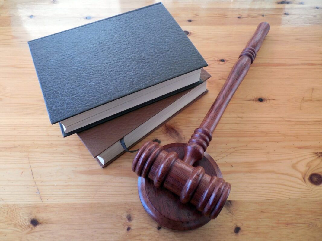 Wooden gavel next to a stack of hardcover books on a honey-colored wooden table, symbolizing law or justice.