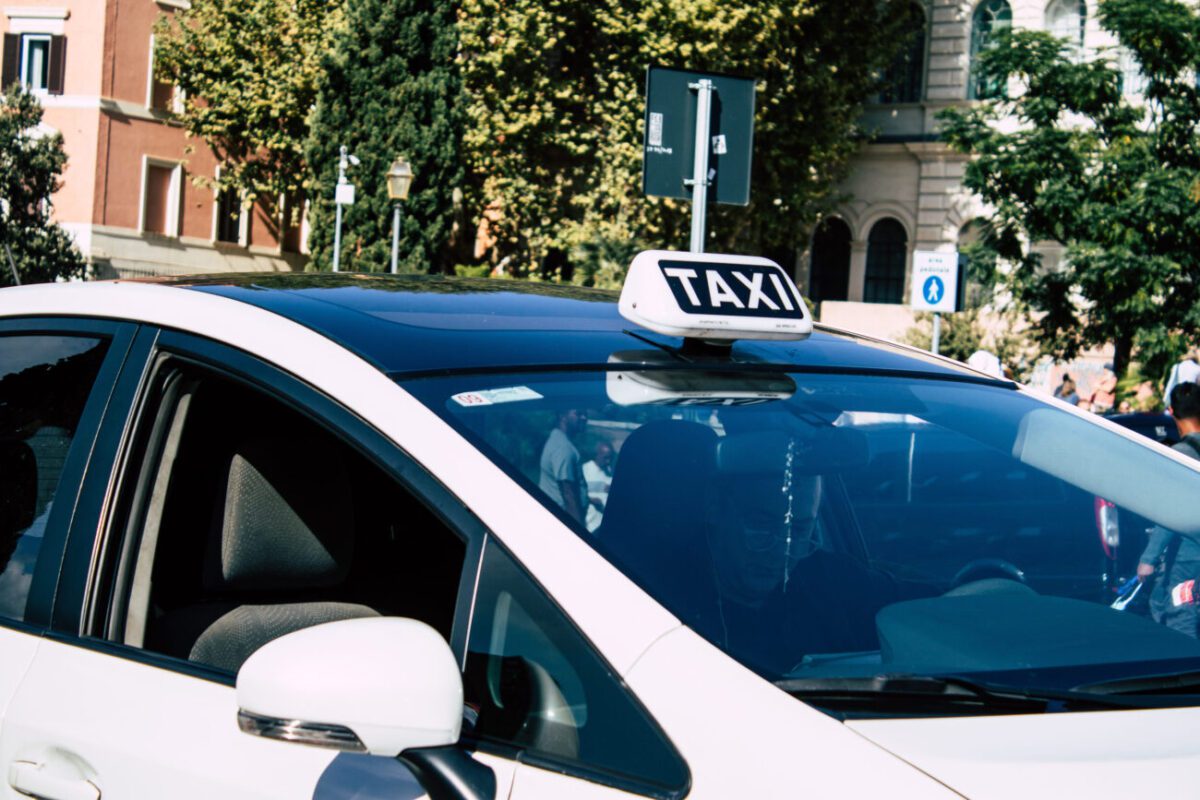 Digiman taxista - IP | diario-economia.com White taxi cab with a rooftop 'TAXI' sign, parked on a city street with buildings and trees in the background.