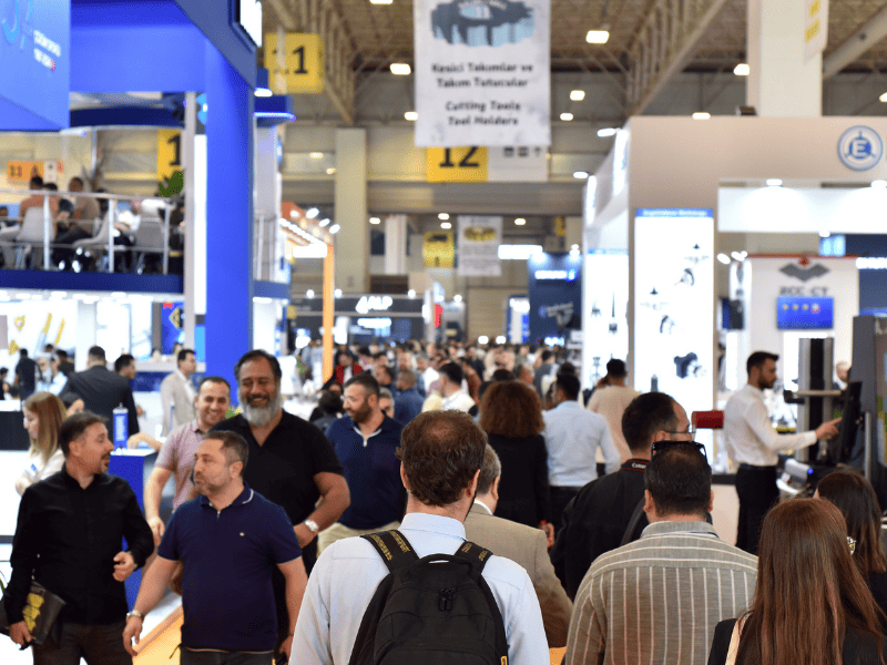 Maktek eurasia - IP | diario-economia.com Crowded trade show hall with attendees walking between booths and large banners overhead.