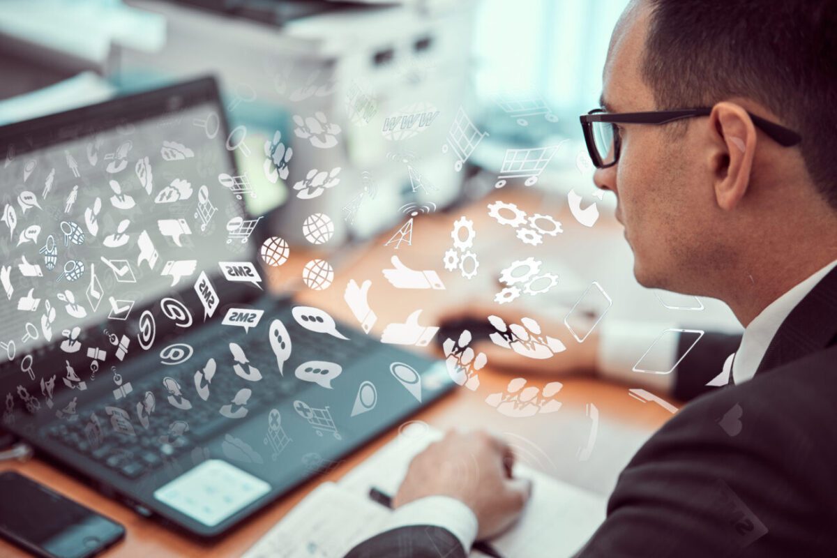Man in a suit with glasses uses a tablet as white app icons stream from the screen, illustrating digital tools and collaboration in an office.