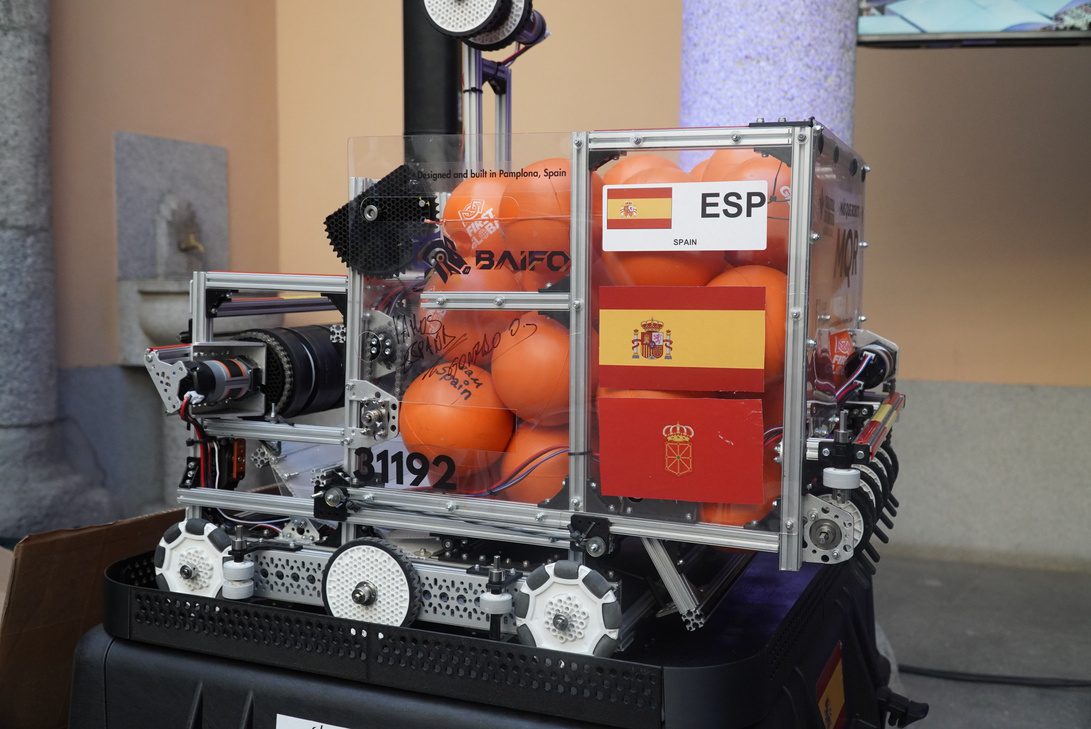 Olimpiadas Robotica Educativa - IP | diario-economia.com Robotic machine on display with orange balls, ESP label, and Spain flag stickers inside a metal frame.