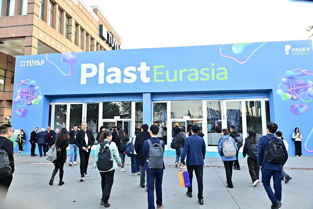 Plast Eurasia - IP | diario-economia.com Crowd of people walking toward the glass doors of a blue Plast Eurasia trade fair entrance. In the background is a building with TÜYAP signage and decorative graphics.