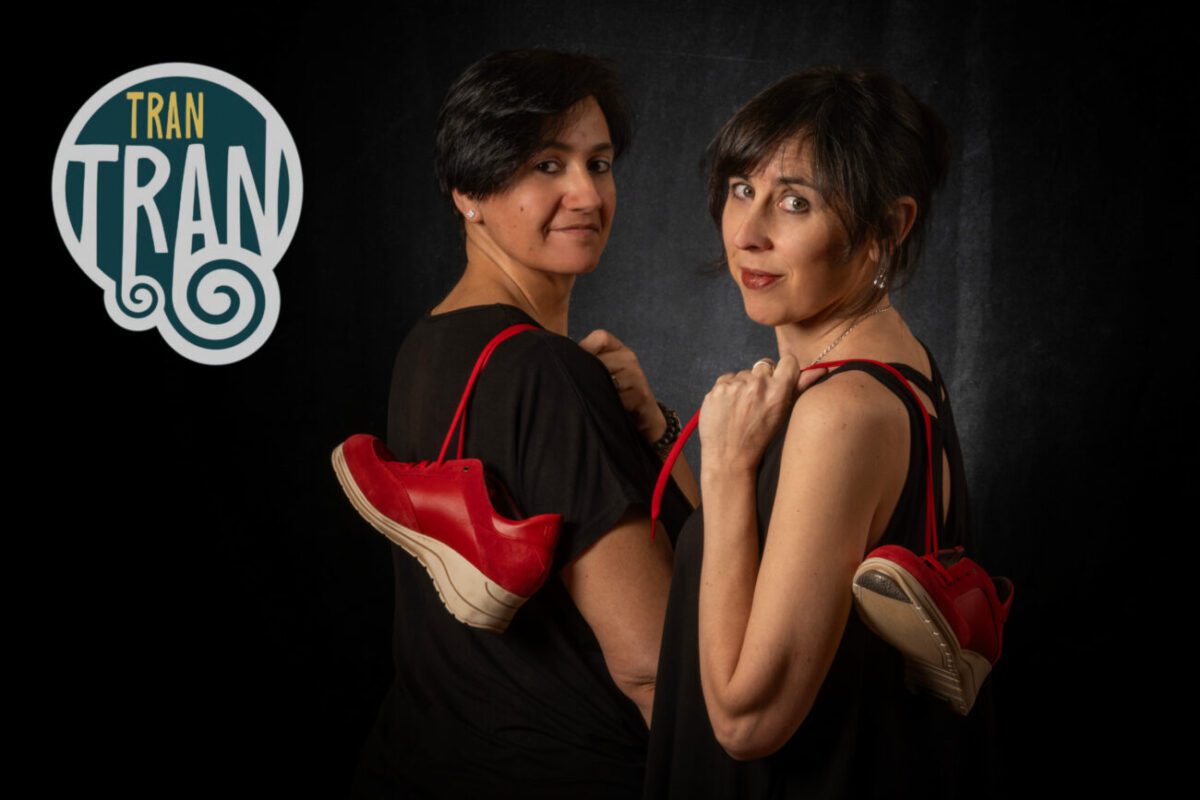 Tran Tran - IP | diario-economia.com Two women in black outfits stand back-to-back with red sneakers hanging over their shoulders; TRAN TRAN logo on the left.
