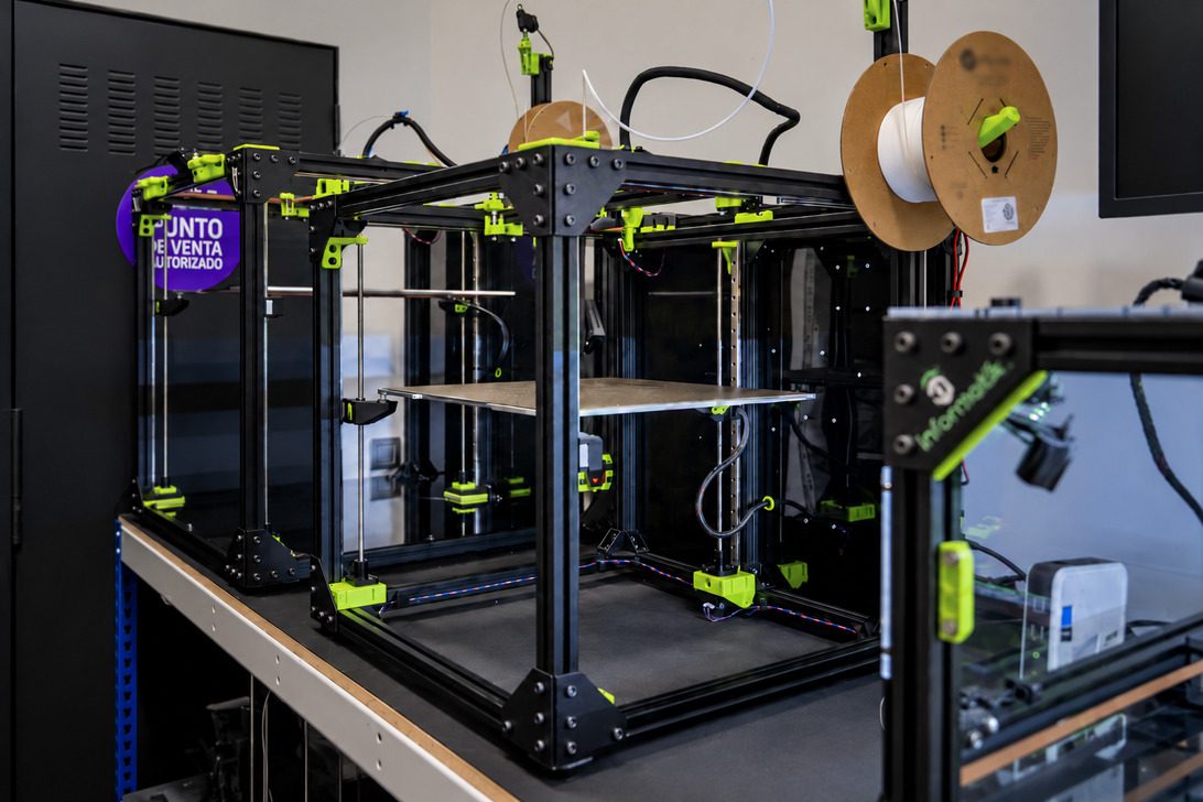 h3d concept - IP | diario-economia.com Open-frame 3D printer with neon-green clamps and spool reels on top, showing a flat build platform inside a glass enclosure.