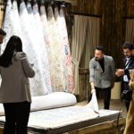 Group of people examines rolled carpets in a showroom, discussing a rug being held up for inspection.