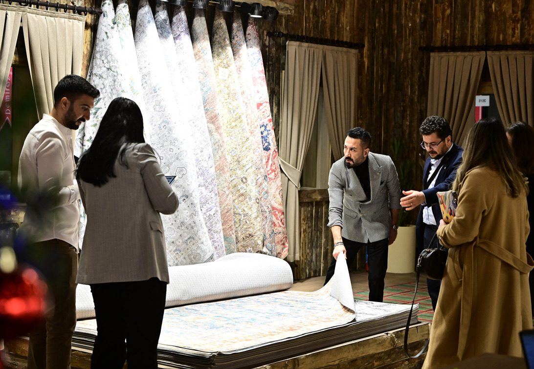 Group of people examines rolled carpets in a showroom, discussing a rug being held up for inspection.